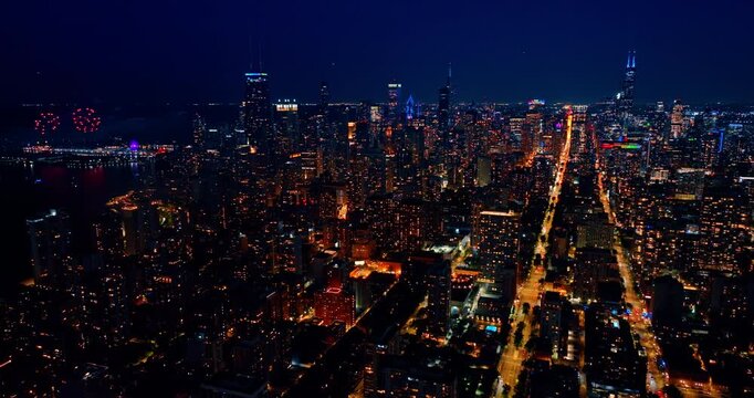 Descend over the luminous streets of Chicago, Illinois, USA at night. Beautiful fireworks splash over the pier in the backdrop.