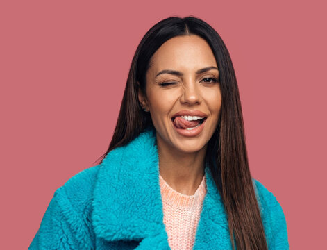 A vibrant studio portrait capturing a moment of pure fun as a beautiful young woman with long dark hair winks and sticks her tongue out playfully