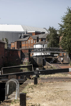 Birmingham, England, United Kingdom - 20 July 2026: View of the historic canal network, featuring brick buildings, a pedestrian bridge, and a person walking along the towpath.