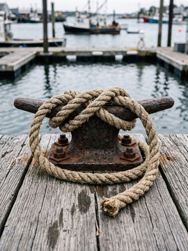 Rope tied around a rusty metal cleat on a wooden harbor dock
