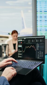 Vertical video: Businessman monitors trading data and stock exchange graphs on a laptop near an airport gate while tracking financial forecasts and investments.
