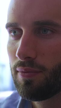 Extreme close-up shot of a handsome bearded man with blue eyes slowly opening his eyes and looking out of a window with a thoughtful and serene expression, feeling peaceful and calm
