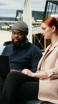 Vertical aspect: Diverse consultants analyze data on a laptop in an airport lounge while preparing for an international meeting and business delegation.