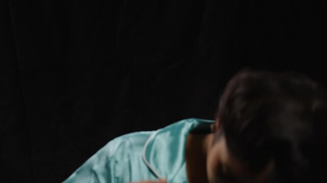 Woman in blue silk pajamas poses in a close-up portrait against a dark backdrop