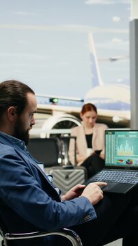 Portrait format: Businessman reviews company reports on a laptop in an airport lounge, analyzing data, KPIs and budget performance before an international meeting and overseas flight.