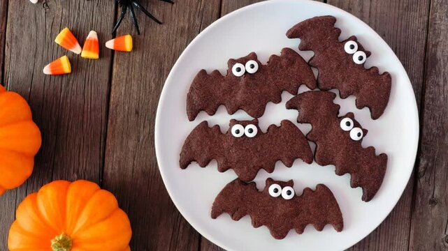 Chocolate Halloween bat cookies. Above view with decor on a dark wood background. Slow rotating zoom motion.