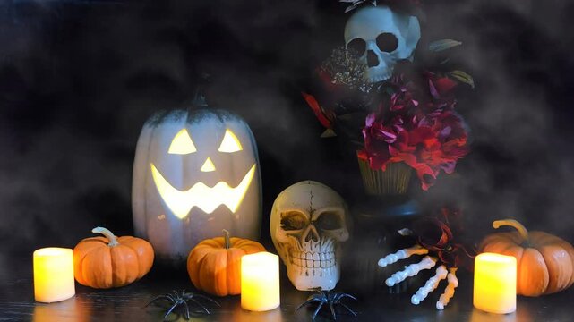Halloween decor night scene with jack o lantern, skulls, flowers and flickering candles on a dark background with rolling fog
