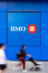 Fototapeta premium Toronto, Canada - June 19, 2026: Pedestrians passing BMO bank logo on blue building exterior