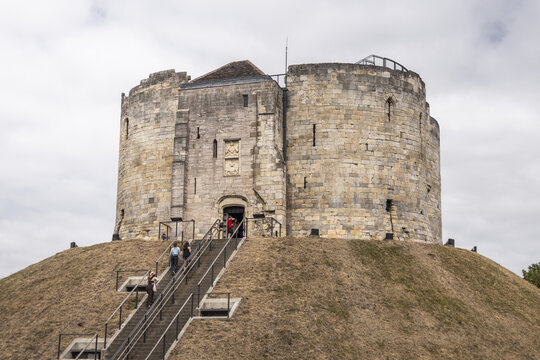York, England - 14 July 2026: View of Clifford's Tower, a historic stone keep on a grassy mound with visitors walking up the stairs under a cloudy sky.