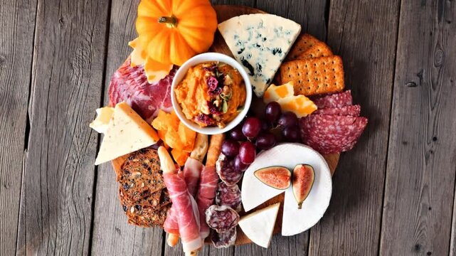 Fall theme charcuterie board. Above view against a dark wood background. Slow rotating zoom motion.