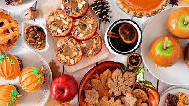 Autumn desserts table scene with various sweet fall treats. Top view over a white wood background. Slow rotating zoom motion.