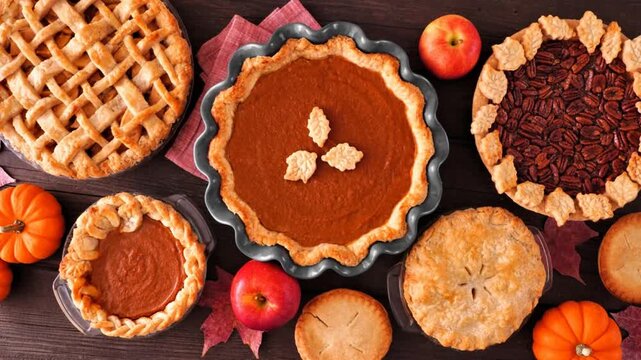 Assortment of homemade fall pies. Apple, pumpkin and pecan. Top down view table scene on a dark wood background. Slow rotating zoom motion.