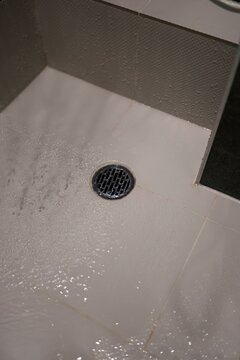 浴室の排水溝。水が流れ込む。白いタイル床。黒いグレーチング蓋。