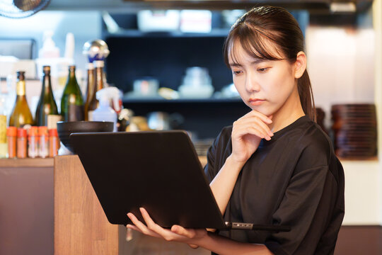 居酒屋で困った顔をしながらパソコンを使う女性店長