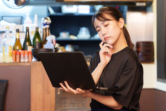 居酒屋で困った顔をしながらパソコンを使う女性店長