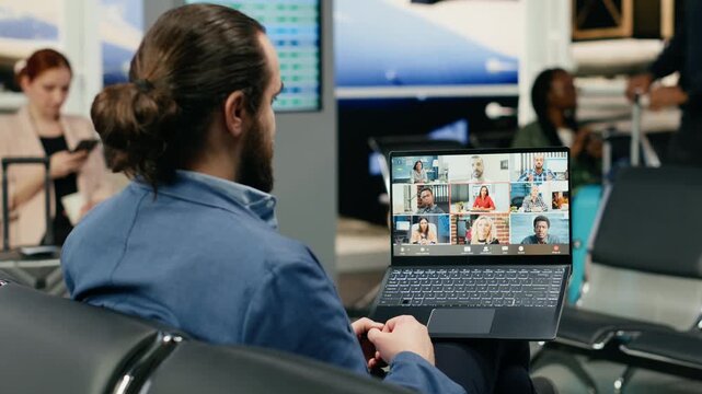 An executive uses a laptop for a video call in an airport lounge, interacting with team members and partners in a virtual meeting during a business trip before his international flight.