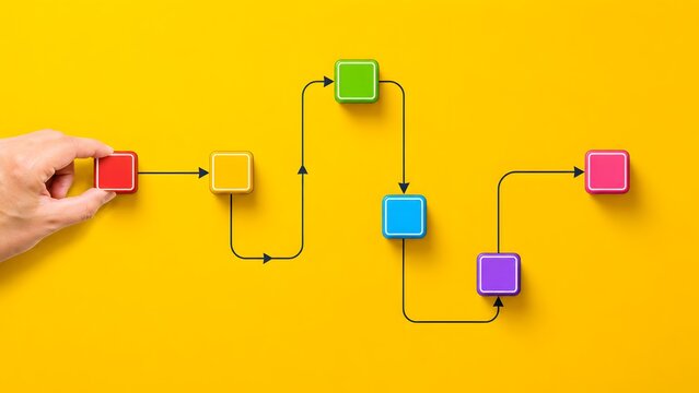 Human hand arranging colorful square blocks connected by arrows on a yellow surface. Concept of workflow optimization and logical process management.