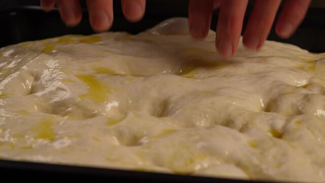 Fingers sink into the soft, airy focaccia dough, brushed with olive oil, on the baking sheet.