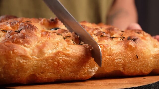 Close-up of hot, crispy olive focaccia being sliced ​​with a bread knife.