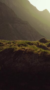 Mountains rise in the background as sunlight sets over grassy fields in the valley. The sky has a warm color, and the landscape showcases natures beauty.