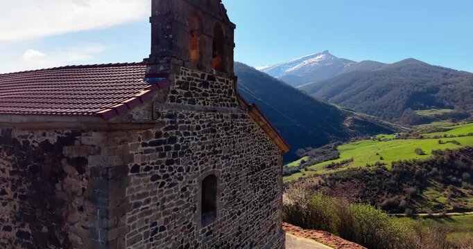 Cinematic rising reveal over a historic stone chapel and its bell tower to a stunning mountain range with snow-capped peaks