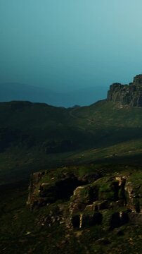 A wide view of a mountain landscape features rocky formations and green hills. The scene captures a clear sky with few clouds. This location is likely in a rural area away from cities.