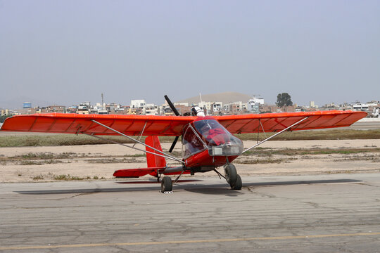 Red Ultralight Aircraft Parked on a Runway with Lima's Hillside Homes in the Background