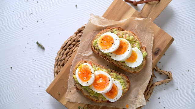 Avocado toast with sliced boiled eggs on wooden board