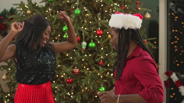 Couple dances and laughs together next to a lit Christmas tree with colorful ornaments.