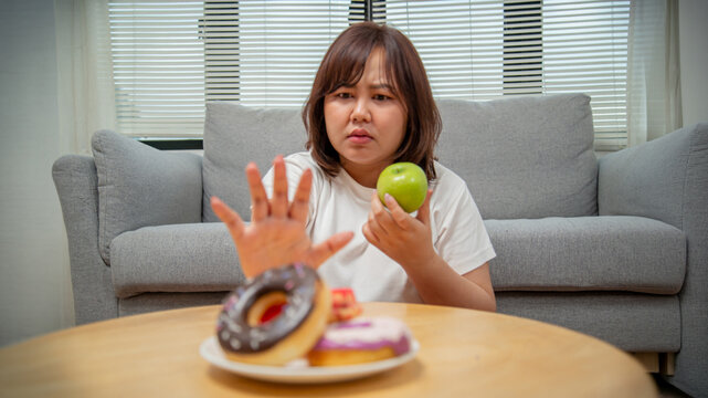 Overweight teenage girl rejecting sweets and choosing fruit for healthy eating, weight loss, obesity prevention, nutrition, and wellness concept.