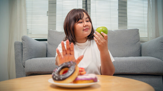 Overweight teenage girl rejecting sweets and choosing fruit for healthy eating, weight loss, obesity prevention, nutrition, and wellness concept.