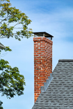 Red brick chimney with metal cap rising above gray shingled roof
