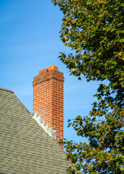 Red brick chimney on a residential shingled roof with a green tree in Boston