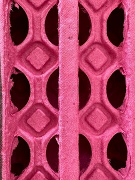 Full frame macro texture of a pink molded pulp egg carton with geometric diamond shapes and oval cutouts, abstract cardboard pattern background.