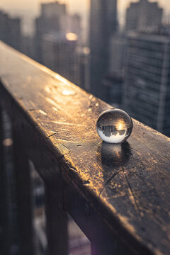 Crystal ball resting on a high balcony railing reflecting an inverted cityscape and sunset glow