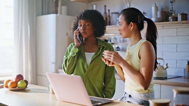 Friends using laptop kitchen. Woman talking phone, roommate drinking coffee.