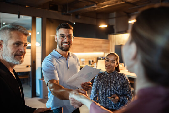 Diverse coworkers greeting with handshake in modern office