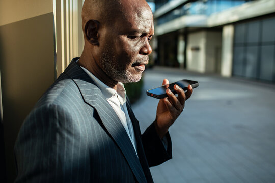 Mature businessman using voice command on smartphone outside office