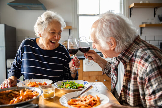 Smiling senior couple toasting red wine at home kitchen table