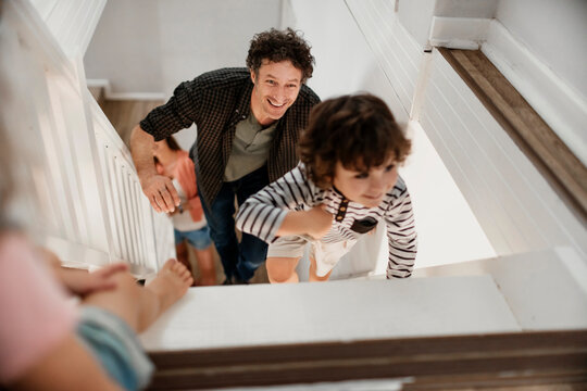 Smiling father and children climbing stairs at home