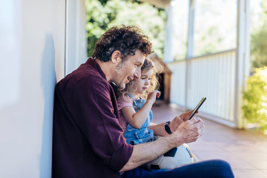 Father and daughter using smartphone on home porch