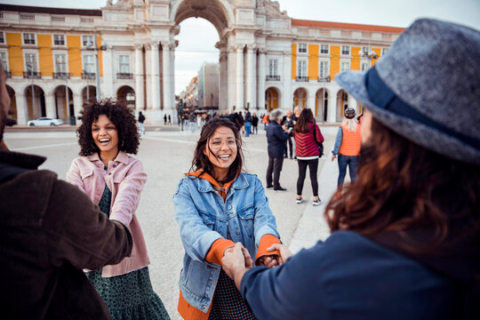 Friends laughing and holding hands at praca do comercio, lisbon, portugal