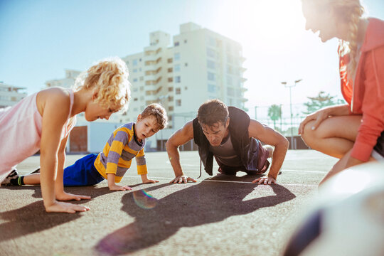 Parents and children doing push-ups on sunny outdoor court