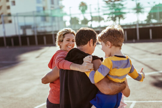 Parents hug and carry son on sunny outdoor sports court