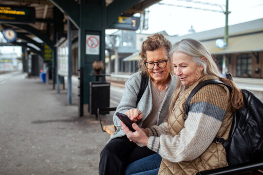 Two senior women checking smartphone at train station