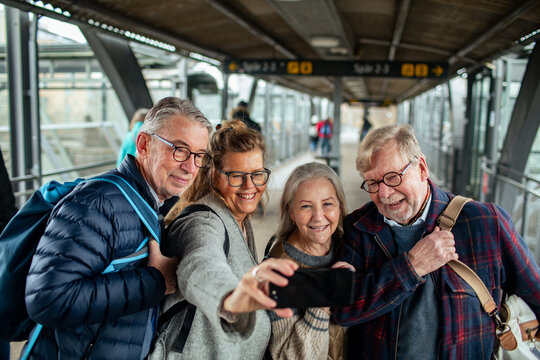 Senior friends taking selfie at train station platform