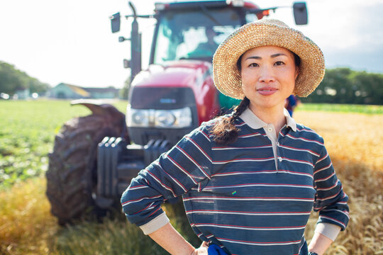 Confident female farmer standing by tractor in sunny field