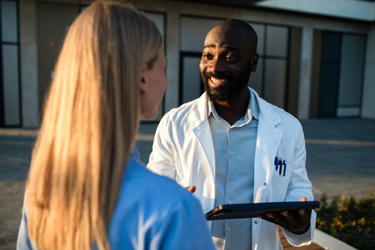 Smiling doctor consulting colleague outdoors at hospital