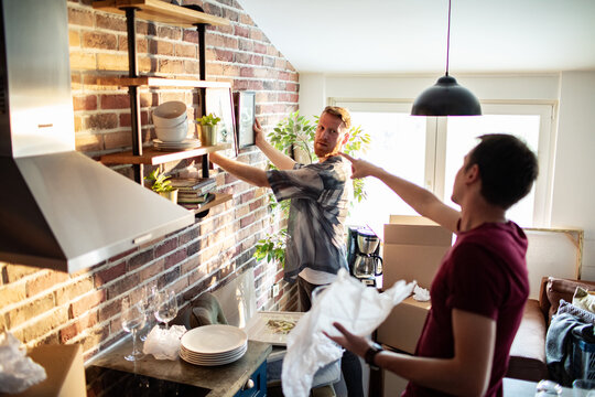 Two men unpacking and decorating kitchen shelves at home