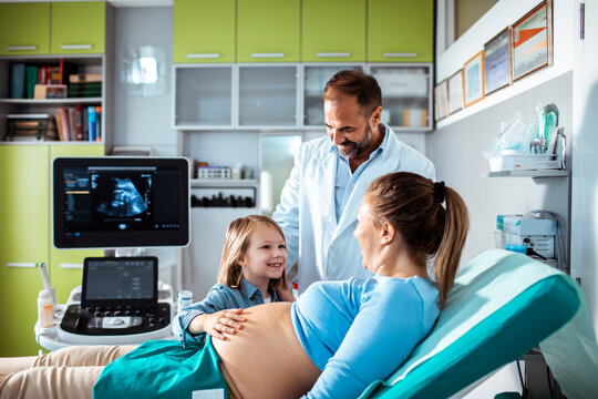 Pregnant mother with daughter and doctor during ultrasound exam in clinic